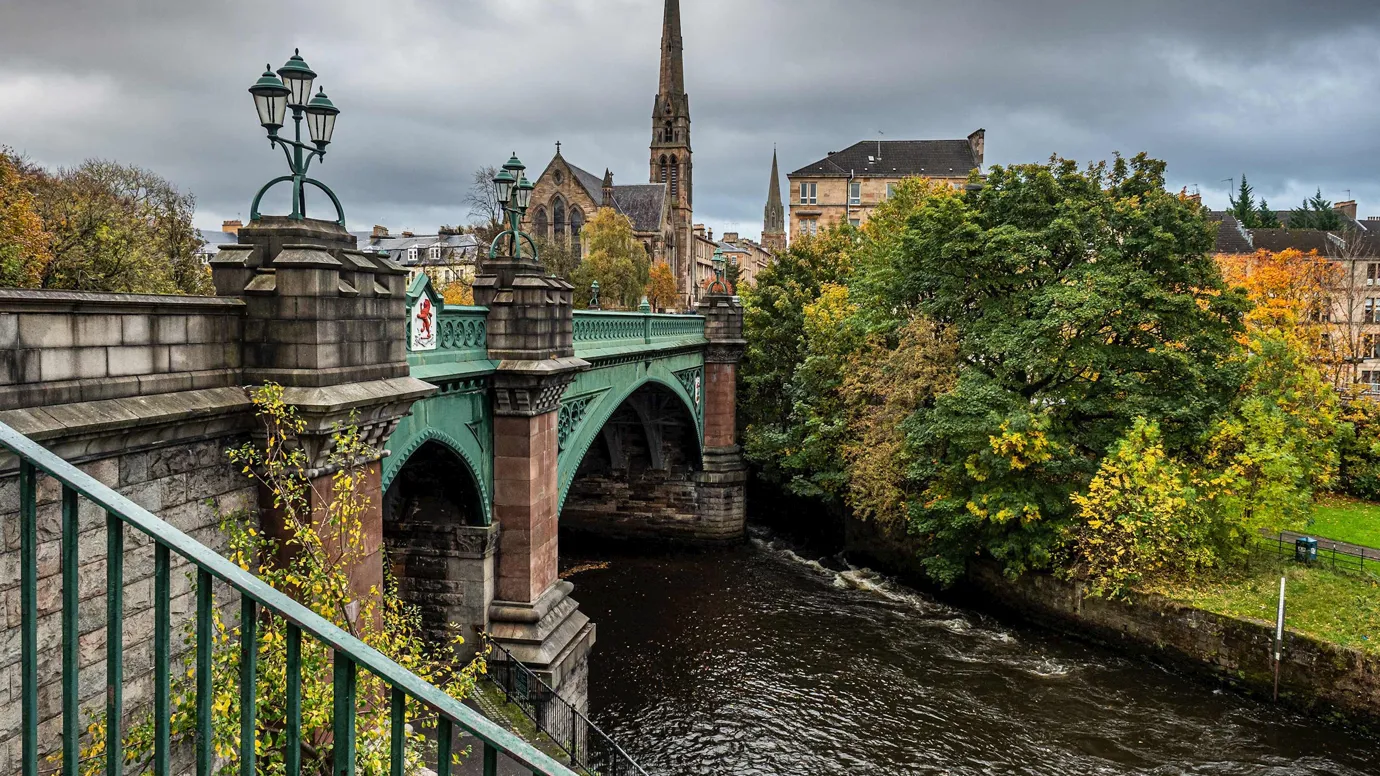 Green iron bridge spanning river with greenery in Glasgow