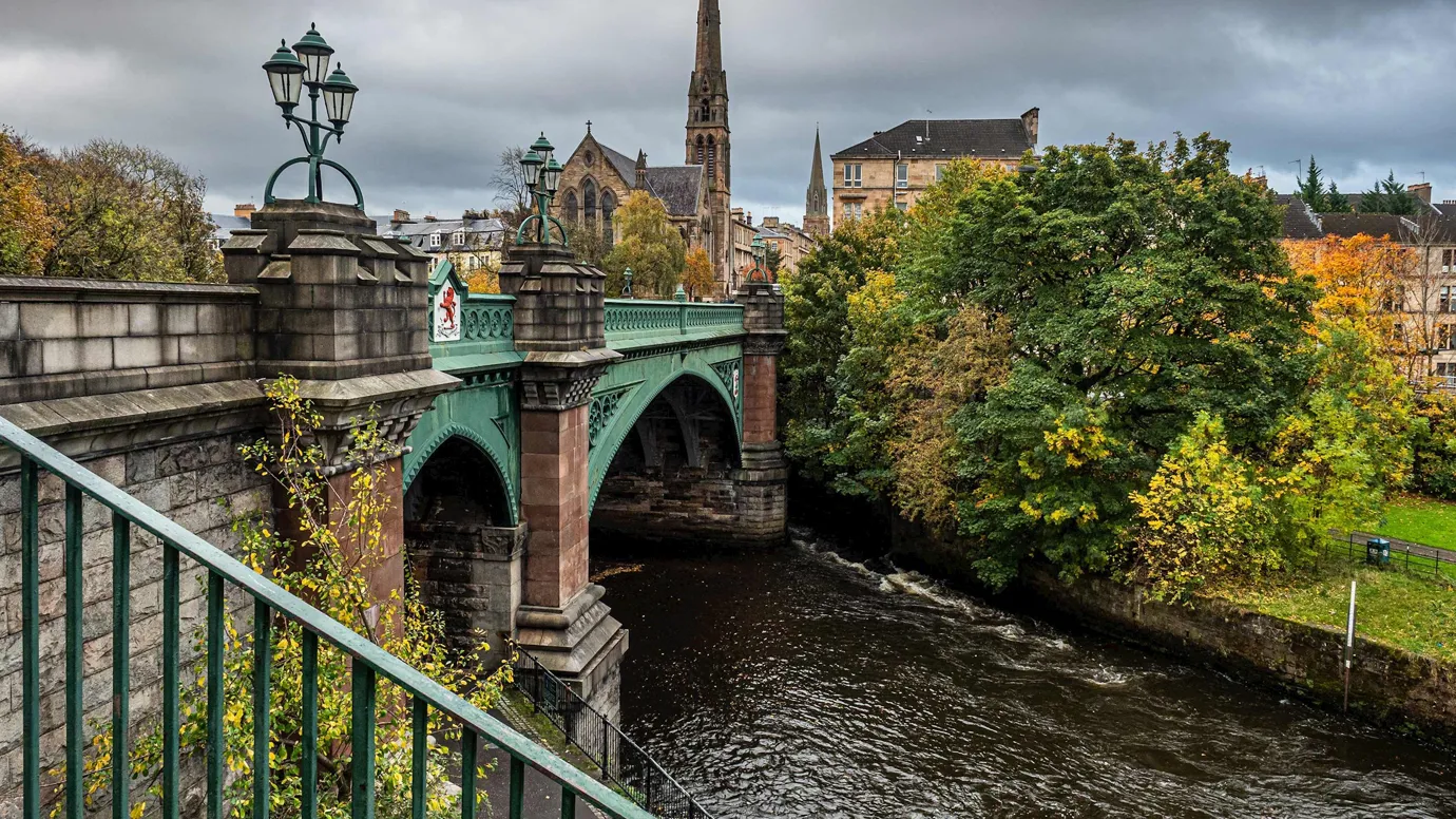 Green iron bridge spanning river with greenery in Glasgow