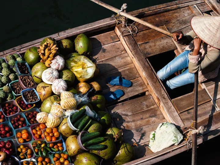 Boxes of vegetables, bread and other food on the front of a wooden boat in Vietnam.