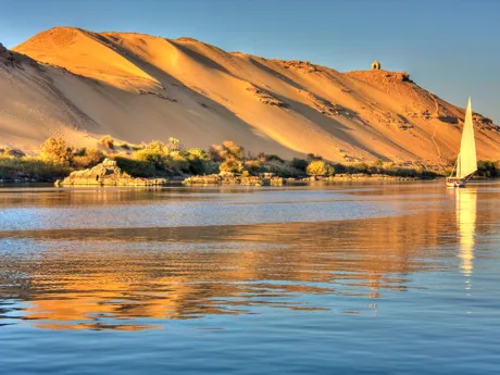 A sailing boat on the Nile River in Egypt. The river bank in a tall sand dune that slopes down to the water.