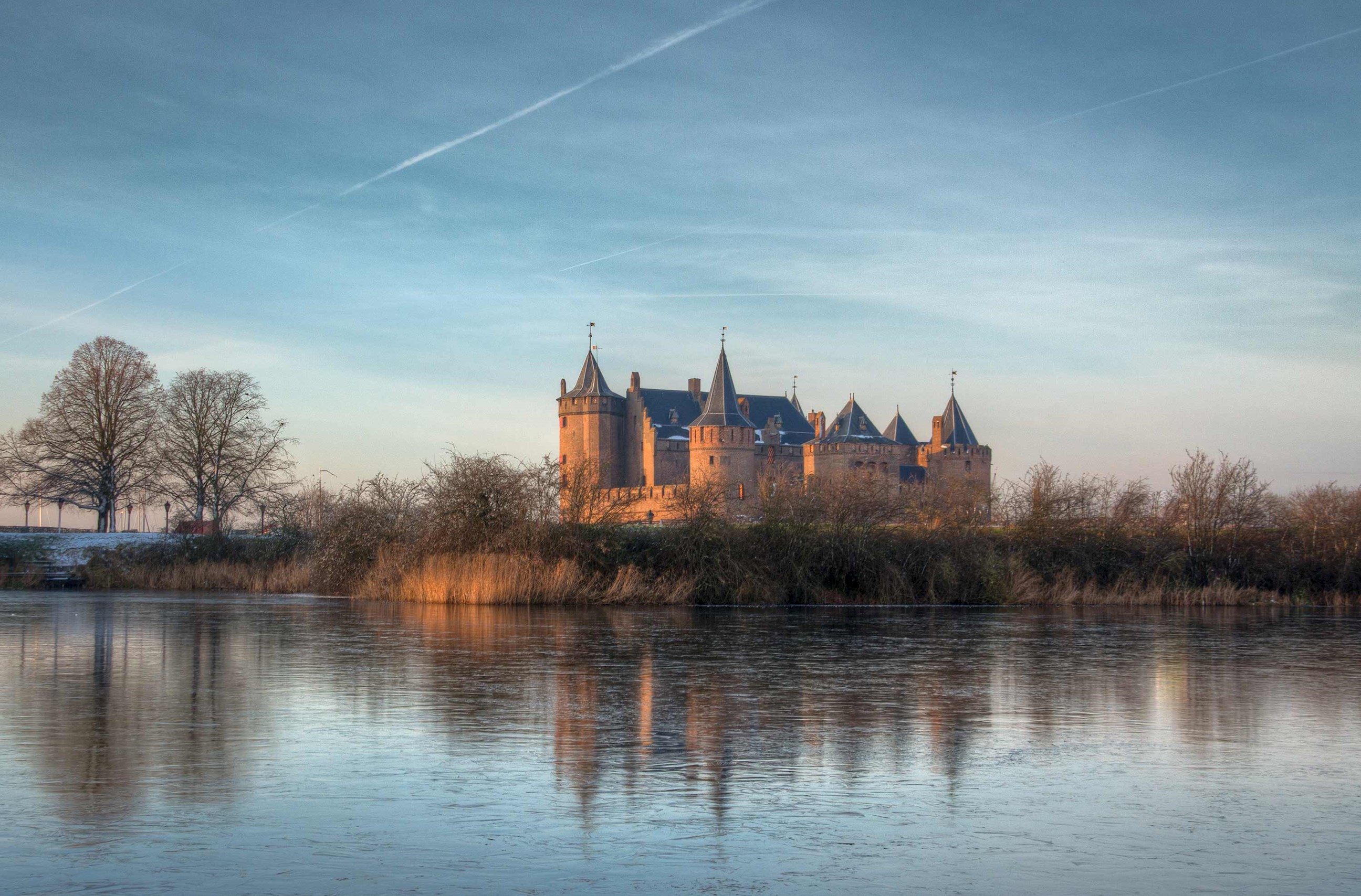 Muiderslot Castle reflected in calm water under blue sky