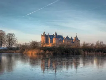 Muiderslot Castle reflected in calm water under blue sky