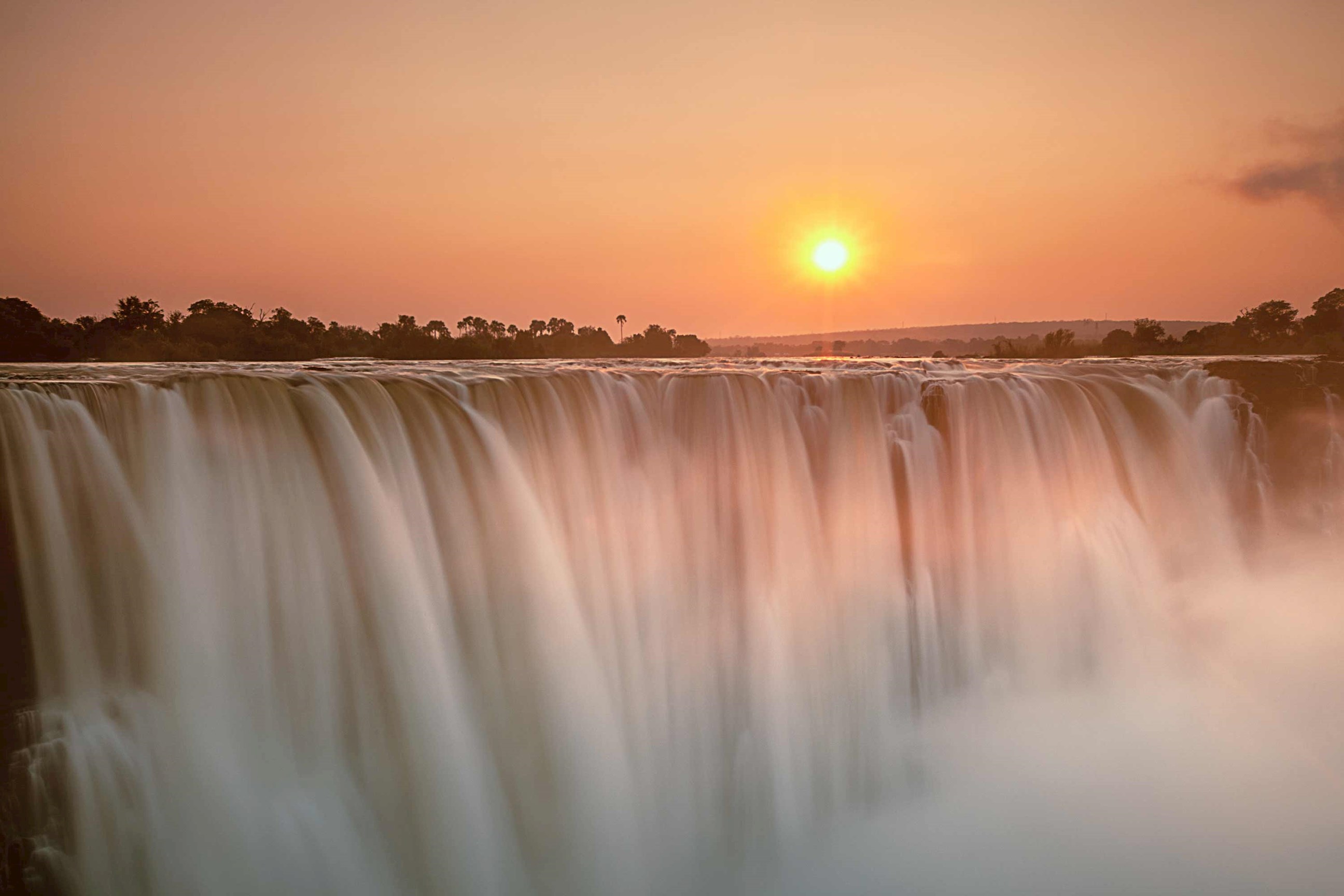 A waterfall flowing at sunset beneath an orange sky in Zimbabwe