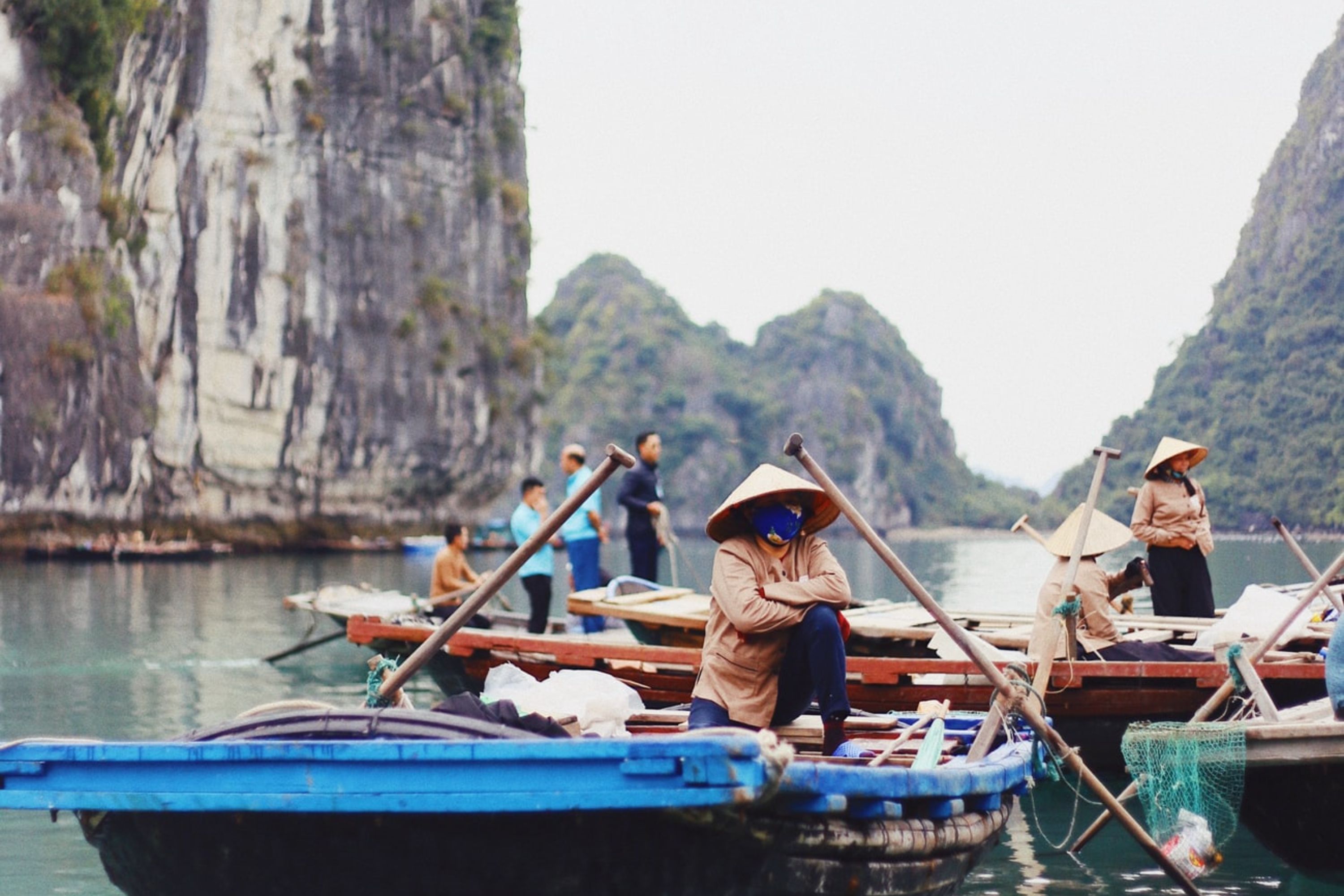 Local people wearing traditional conical hats on fishing boats in Halong Bay, Vietnam.