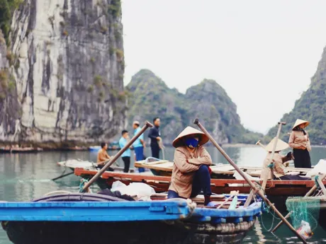 Local people wearing traditional conical hats on fishing boats in Halong Bay, Vietnam.