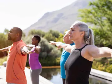 Group practicing outdoor yoga with mountain view and greenery