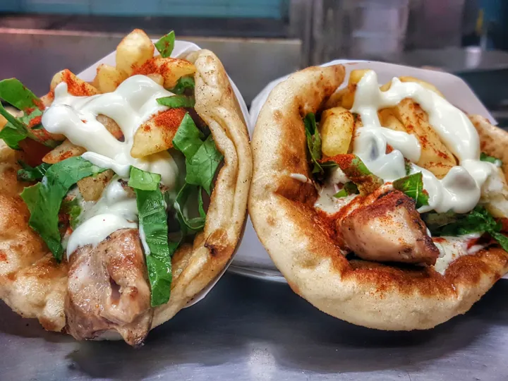 Two Greek flatbreads with meat, potato and green garnishes on them. A popular food in Greece.