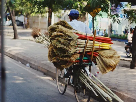 A man riding a bicycle with a stack of brooms piled up on the back ready for markets Siem Reap, Cambodia