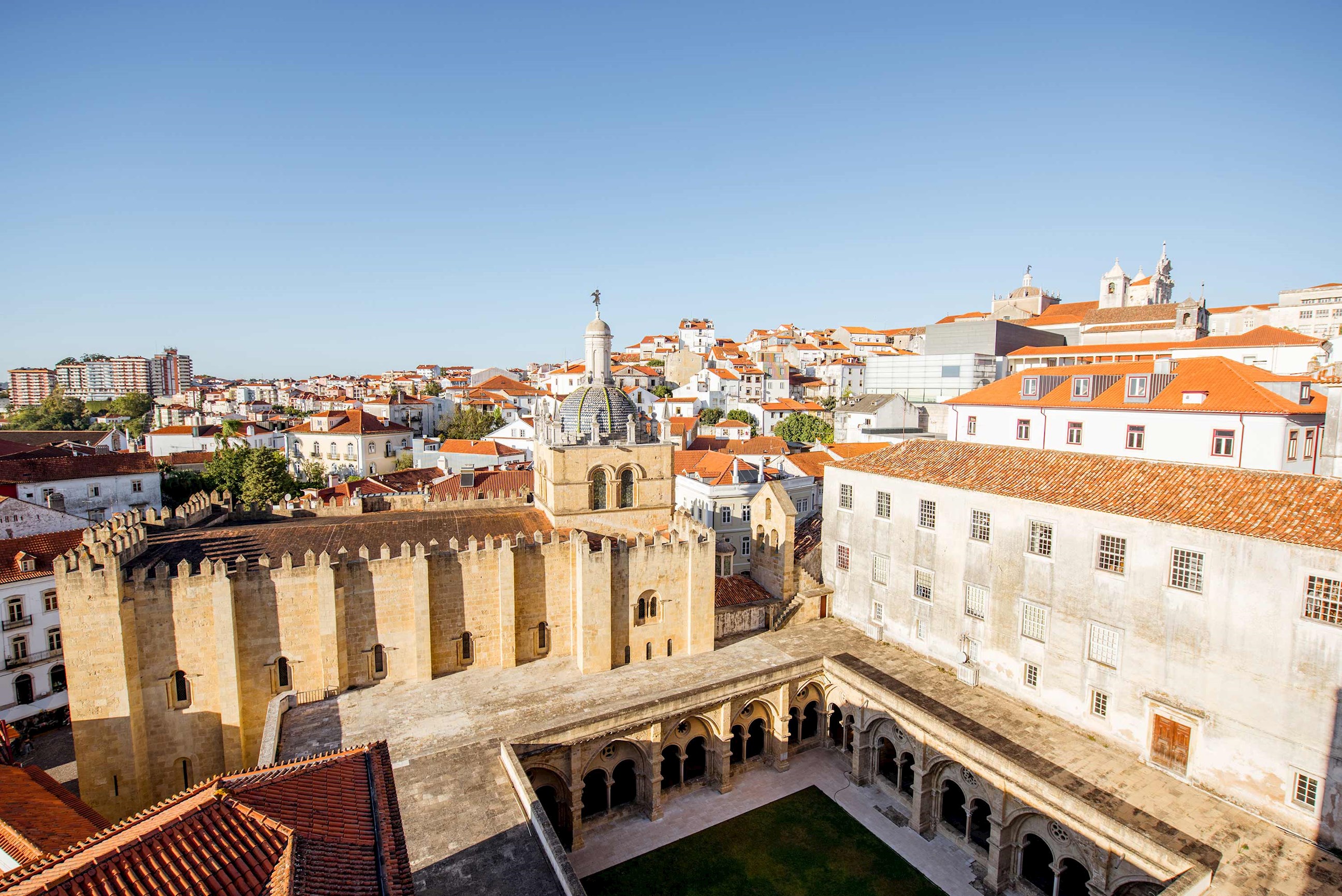 Stone buildings with courtyard and city rooftops in background in Coimbra, Portugal