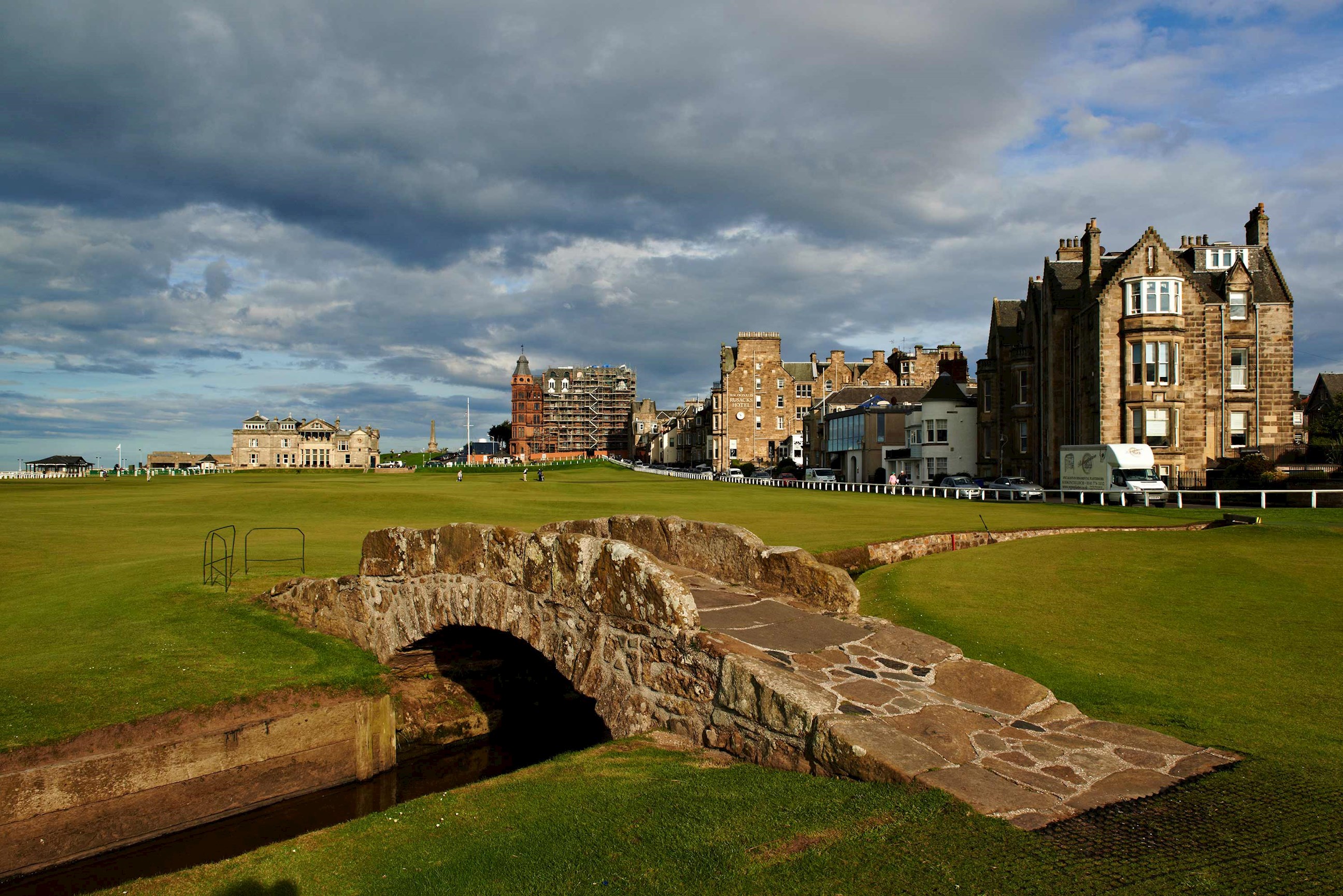 Stone footbridge on golf course with historic buildings in background in St Andrews, Scotland