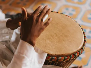 Close-up of hands playing a traditional African drum with woven rim