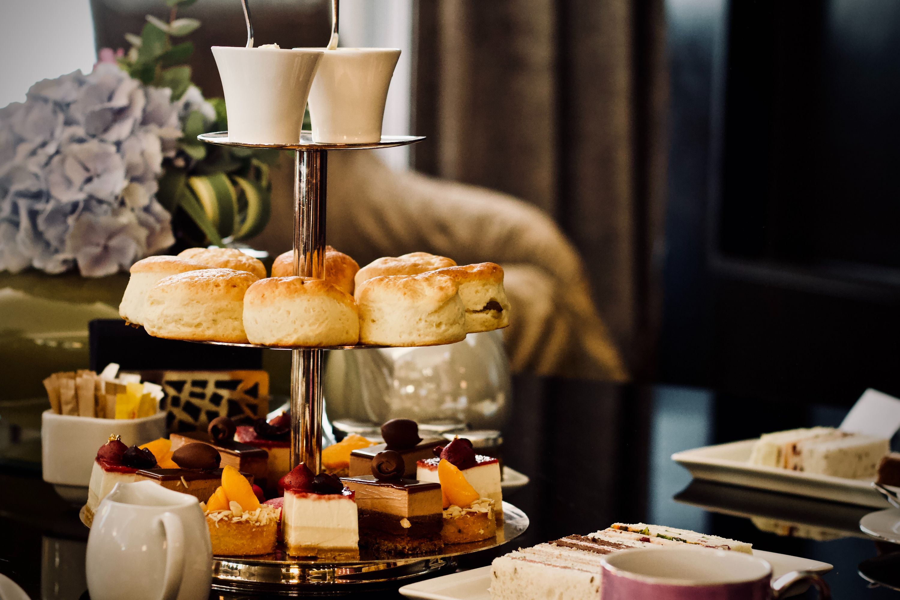 A tiered cake stand holding mini cakes, scones and sandwiches making up an English afternoon tea.