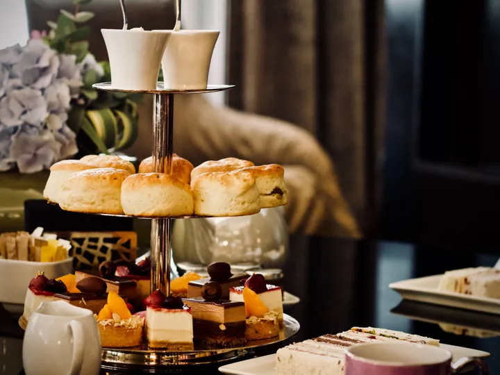A tiered cake stand holding mini cakes, scones and sandwiches making up an English afternoon tea.
