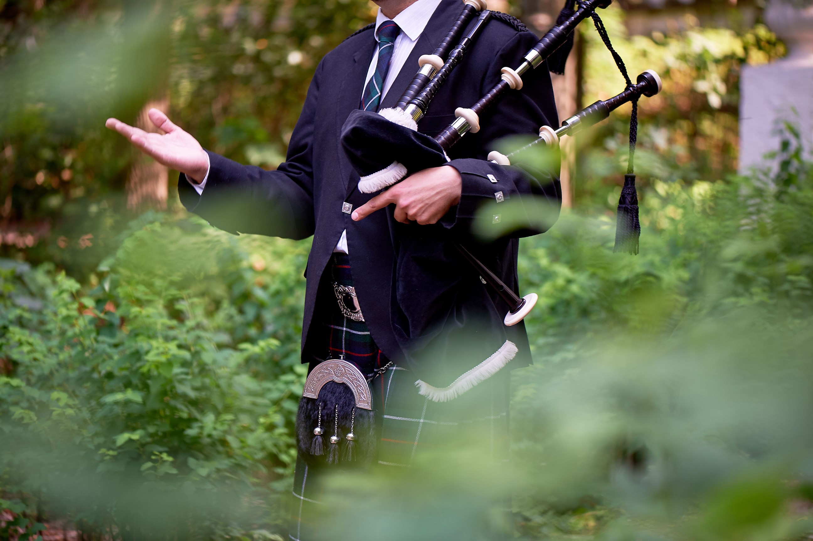 Person holding Scottish bagpipes in traditional attire outdoors