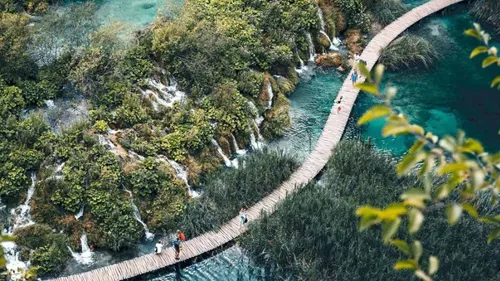 The aerial view of people walking across a bridge over a Plitvice lake in Croatia