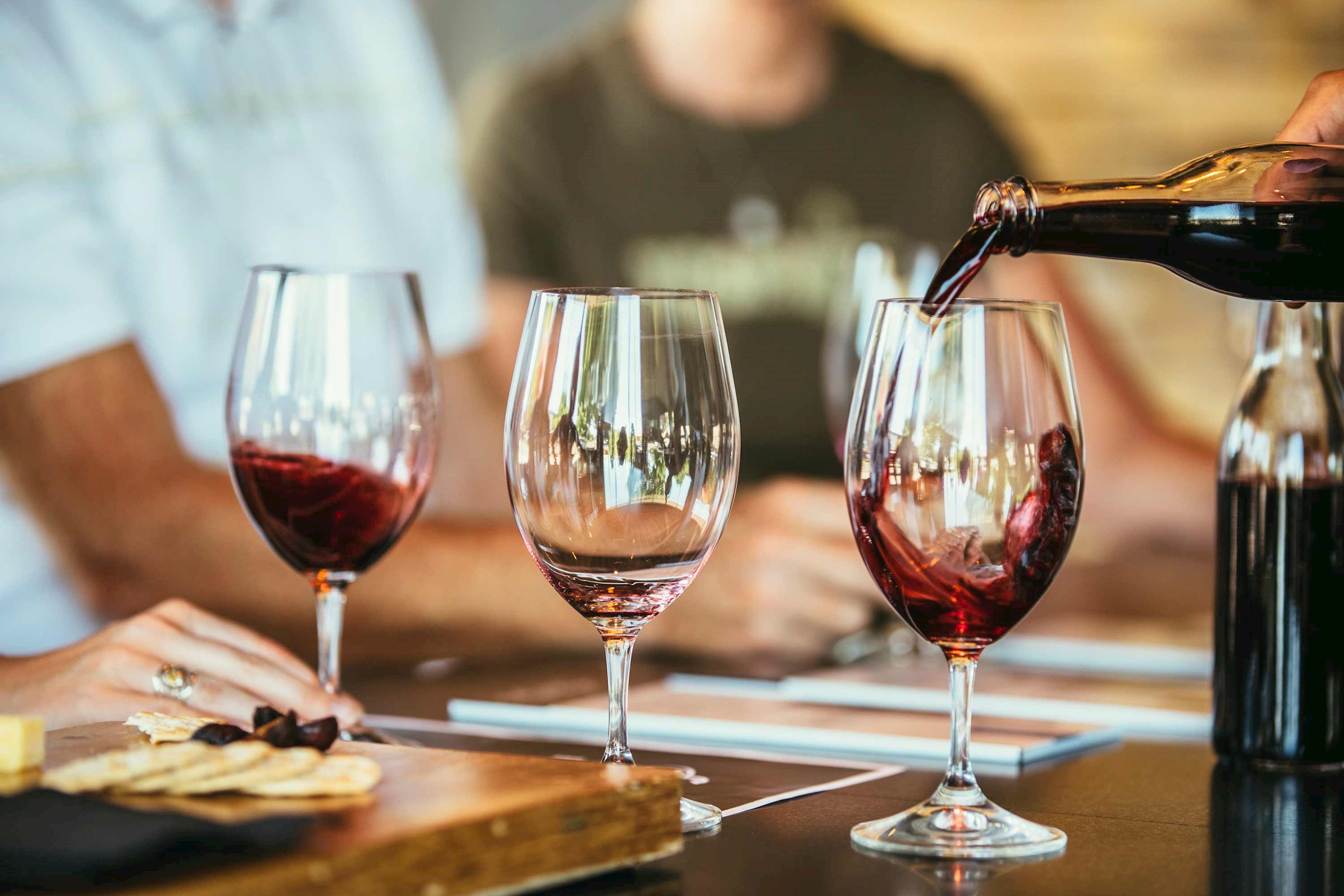 Red wine being poured into glass during tasting with snacks on table